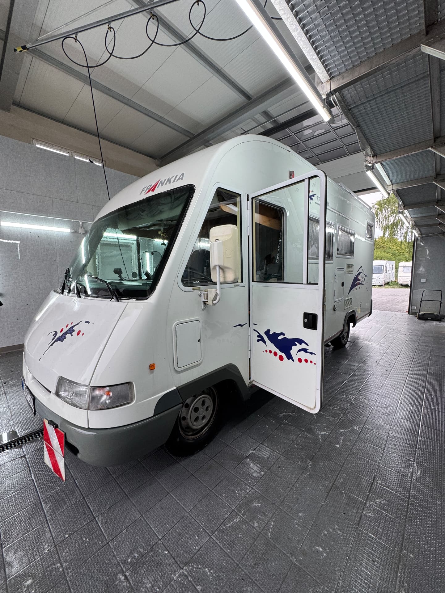 Wohnmobil in der Waschhalle mit offener Tür und gut beleuchtetem Arbeitsbereich