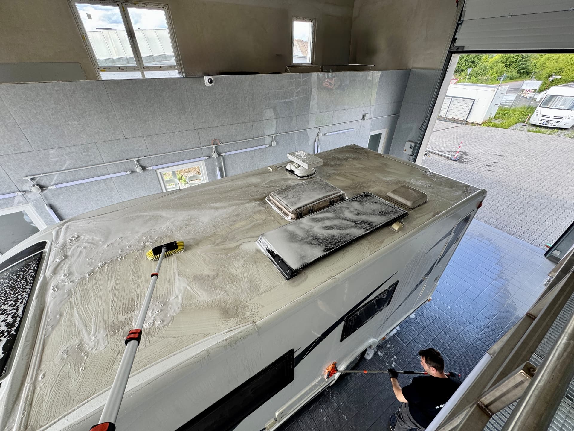 Wohnmobil in der hell beleuchteten Waschhalle mit großer Rolltoreinfahrt