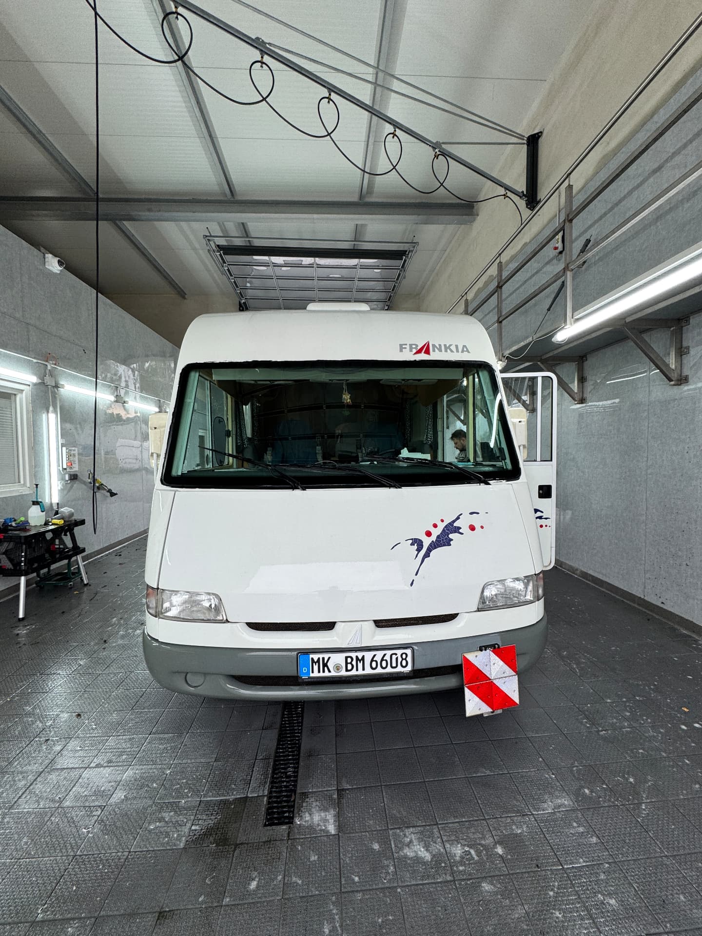 Großes Wohnmobil frontal in der Waschbucht, mit geöffneter Aufbautür und Arbeitswagen daneben